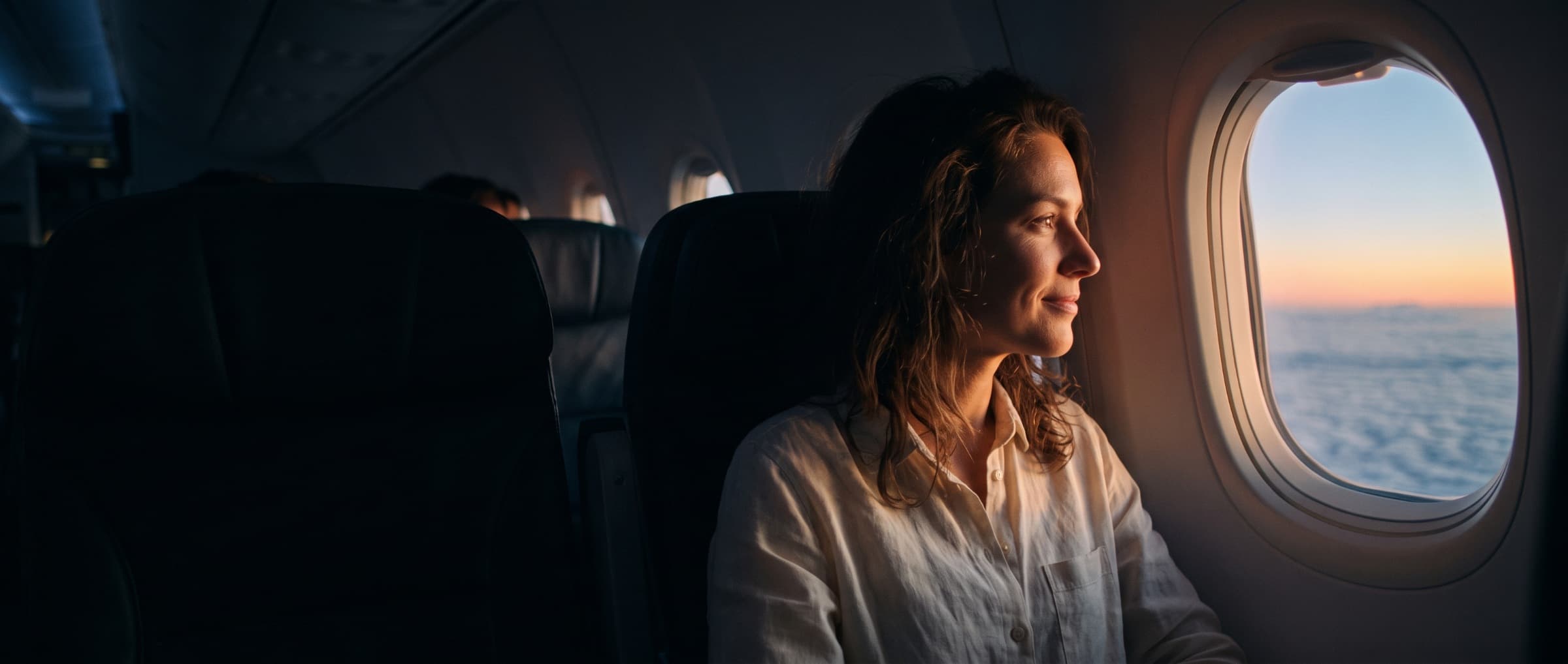 Traveler smiling at a sunrise above the clouds from an airplane window seat